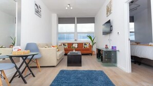 A compact living space with a sofa, a coffee table, a TV, and a bed. - Flat 310 beautiful one bed apartment (Smethwick)