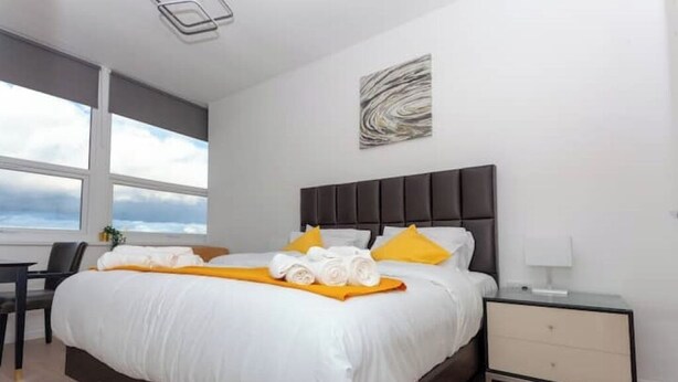 A modern hotel room with a large bed, a bedside table, a nightstand, and a window with a view of the sky. - Flat 310 beautiful one bed apartment (Smethwick)