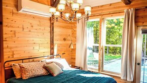A wooden-paneled bedroom with a bed, a chandelier, and a large window with curtains. - New Converted 3BR, 2BA barn, in wild, wonderful West Virginia with AC, WiFi (Triadelphia)