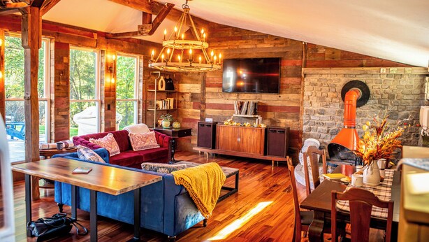 A cozy living room with a blue sofa, wooden flooring, a fireplace, and a television mounted on a stone wall. - New Converted 3BR, 2BA barn, in wild, wonderful West Virginia with AC, WiFi (Triadelphia)