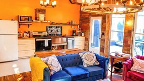 A cozy living room with a blue sofa, wooden floor, and a kitchen area with a microwave and coffee maker. - New Converted 3BR, 2BA barn, in wild, wonderful West Virginia with AC, WiFi (Triadelphia)