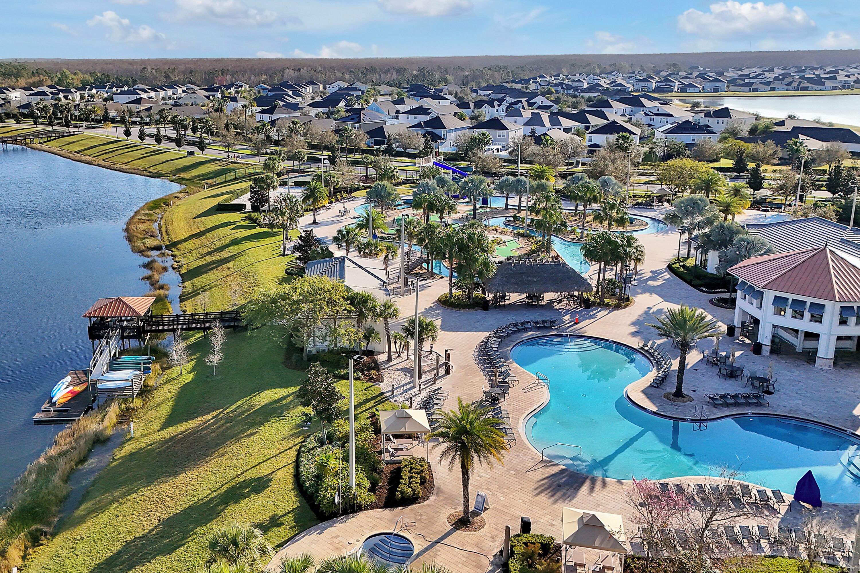 An aerial view of a resort with a large swimming pool, a dock with boats, and a lake.
