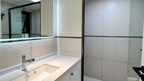 Ein modernes Badezimmer mit einem weißen Waschtisch, einem großen Spiegel und einer Duschkabine aus Glas.