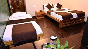 A hotel room with two beds, wooden headboards, a nightstand with a phone, and a small table with a plant and a coffee maker. - JAYA PARADISE Murdeswar (Bhatkal)