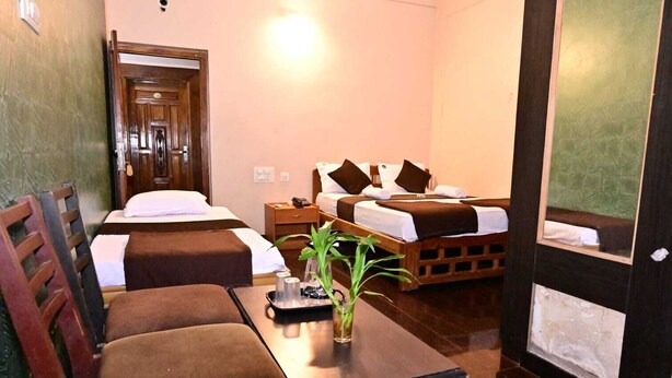 A hotel room with two beds, a wooden desk, a chair, a small table, and a potted plant. - JAYA PARADISE Murdeswar (Bhatkal)