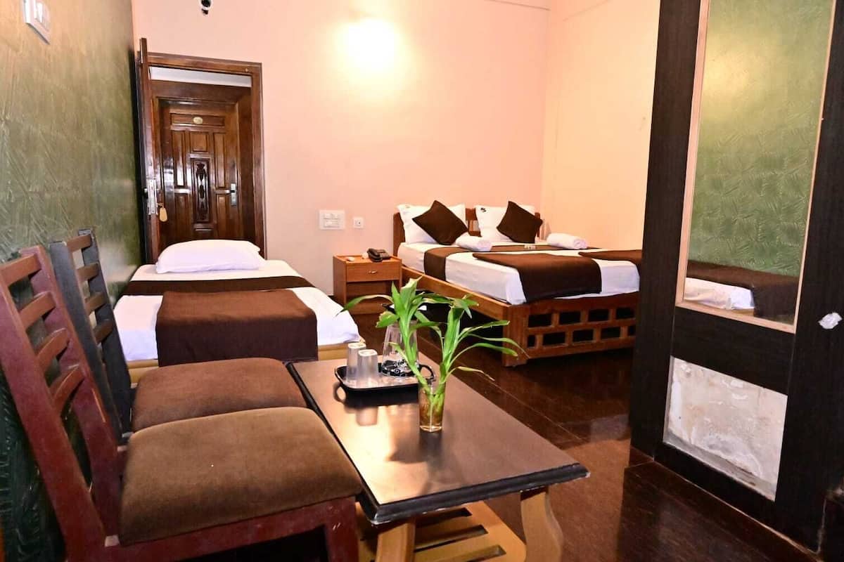 A hotel room with two beds, a wooden desk, a chair, a small table, and a potted plant.