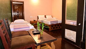 A hotel room with two beds, a wooden table, a chair, and a small plant. - JAYA PARADISE Murdeswar (Bhatkal)