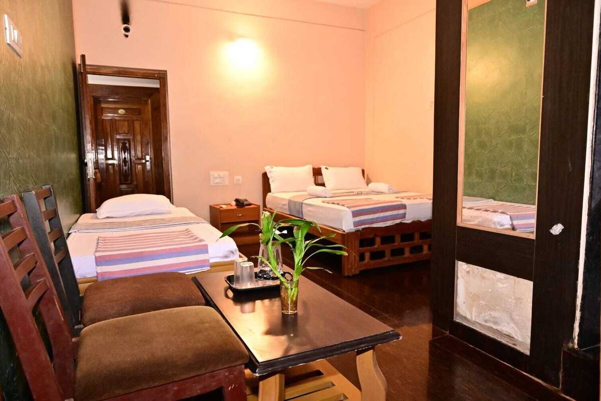A hotel room with two beds, a wooden table, a chair, and a small plant.