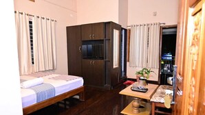 A compact hotel room with a bed, a small table with a kettle, a cabinet, and a view of the street outside. - JAYA PARADISE Murdeswar (Bhatkal)