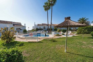 A pool area with a fenced pool, palm trees, and a thatched umbrella.