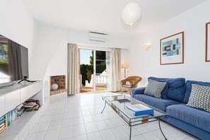 Un salon moderne avec un canapé, une table basse en verre, un fauteuil en osier et un téléviseur.