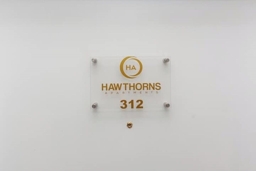 A sign for Hawthorns Apartments, number 312, with a gold logo and text.