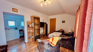 A living room with a sofa, a wooden cabinet, a television, and a kitchen area with a window.