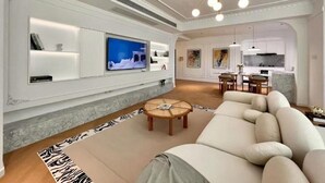 Un salon moderne avec un grand téléviseur à écran plat, un canapé, une table basse et une cuisine en arrière-plan.