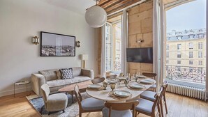 Uma sala de jantar com uma mesa redonda posta para seis pessoas, um sofá e uma TV na parede.