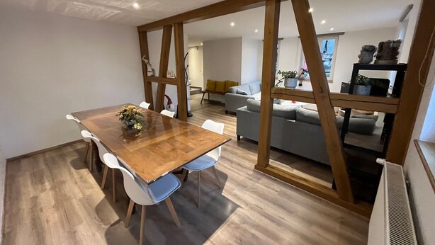A modern dining area with a wooden table and chairs, a sofa, and a radiator.