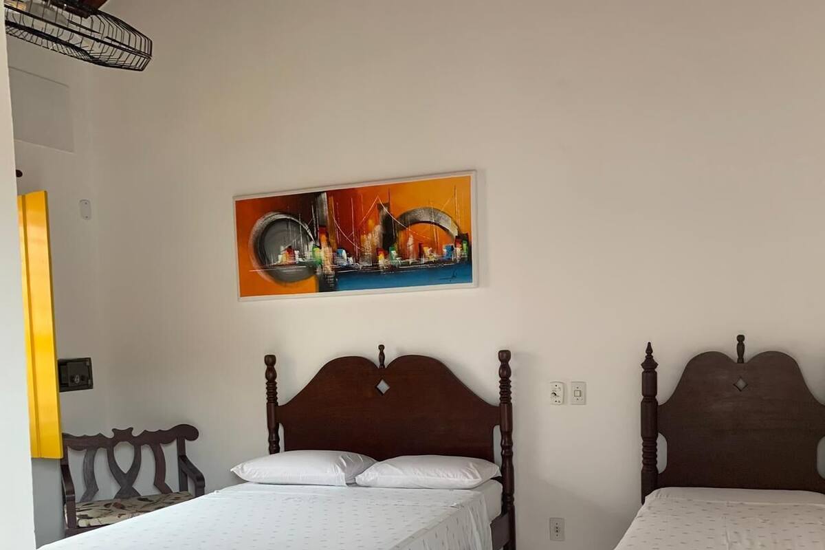 A room with two wooden beds, a colorful painting on the wall, and a tiled floor.