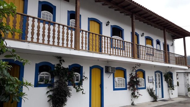 A two-story building with yellow doors and blue window frames, a balcony with a wooden railing, and air conditioning units on the exterior. - Recanto da Cleide (Paraty)