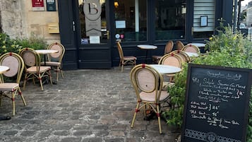 A hotel entrance with outdoor seating, a chalkboard menu, and a sign reading 'LE PETIT BELTON HOTEL.'