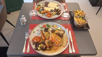 A dining table with two plates of food, salt and pepper shakers, a glass of water, and a basket of fries.