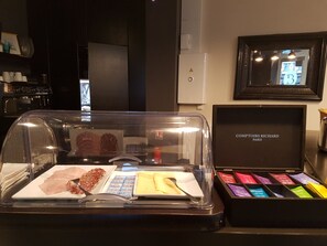 Un présentoir rempli de divers fromages et de charcuteries, un tableau encadré accroché au mur et une enseigne indiquant « Comptoirs Richard Paris ».