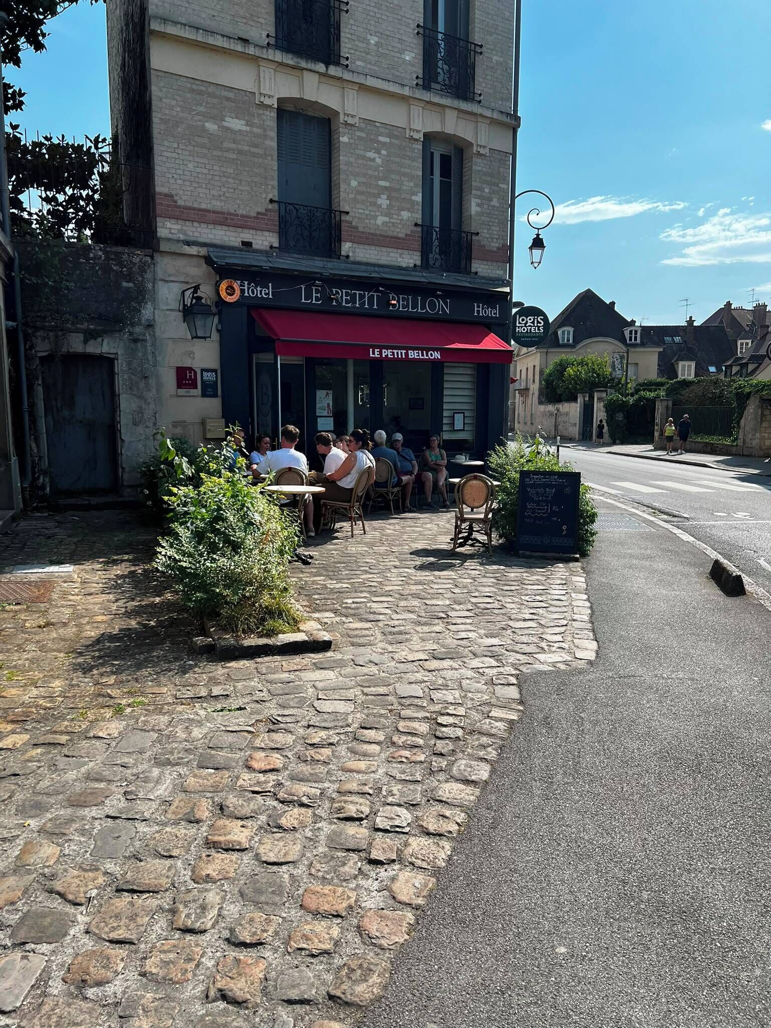 Un bâtiment avec un auvent rouge sur lequel on peut lire « LE PETIT BELTON HOTEL », et, au fond, une enseigne « LOGIS HOTELS ».