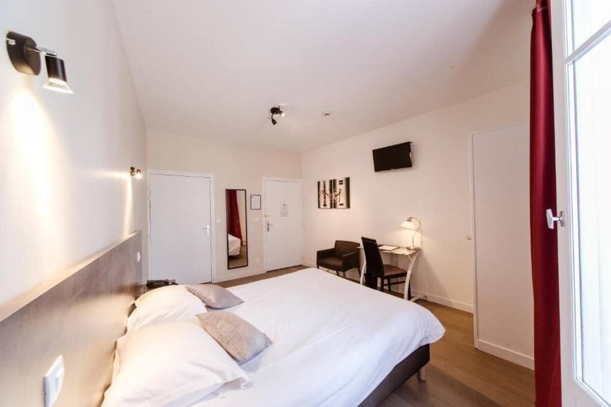 A hotel room with a large bed, a desk, a chair, and a TV on the wall.