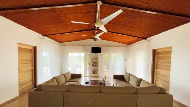A spacious living room with a large sectional sofa, a ceiling fan, and a bookshelf. - Private Retreat w/ Pool, Stunning Views & Wildlife (Vieques)