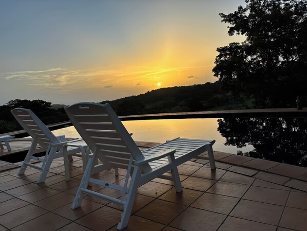 Dos sillones blancos mirando un cuerpo de agua tranquilo con un atardecer al fondo.