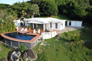 Una casa moderna con piscina, mobiliario exterior y un jardín cuidado.