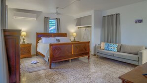 Un dormitorio con una cama de madera, un sofá, una mesita de noche, una lámpara y una ventana con cortinas.