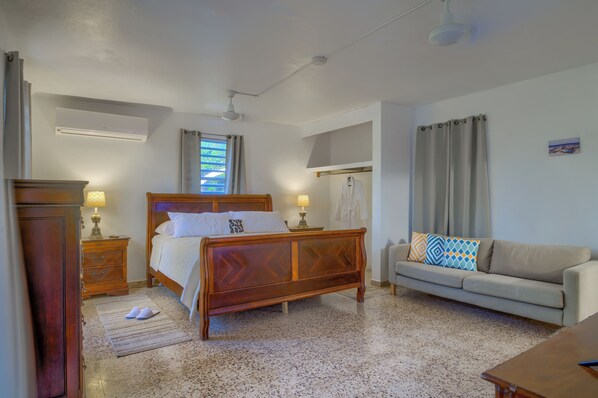 A bedroom with a wooden bed, a sofa, a nightstand, a lamp, and a window with curtains. - Private Retreat w/ Pool, Stunning Views & Wildlife (Vieques)