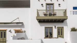 Un bâtiment blanc doté d’un balcon, d’un escalier et d’une porte avec des volets verts.