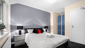 Quarto moderno com cama grande, mesas de cabeceira, criado-mudo e guarda-roupa.