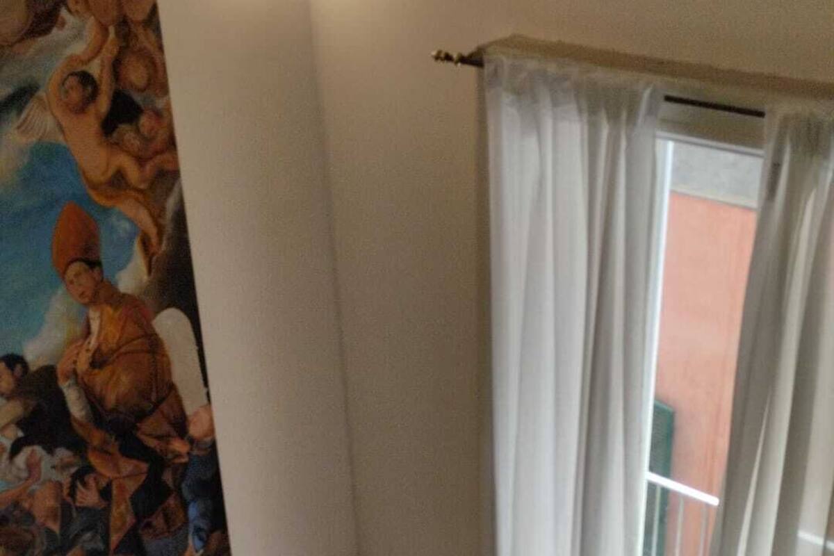 A room with a dark sofa, a painting on the wall, and a window with white curtains.