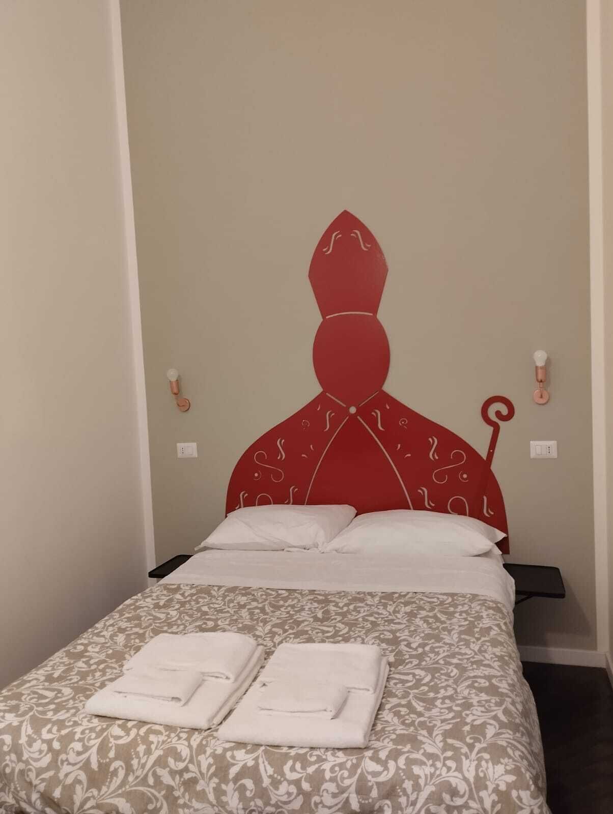 A bed with a red headboard, white pillows, and a patterned bedspread. There are two folded towels on the bed.