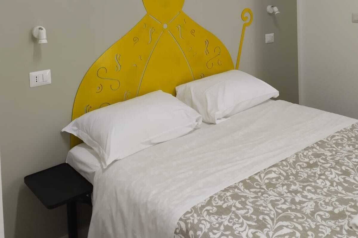 A bed with white bedding and a yellow headboard with a unique design.
