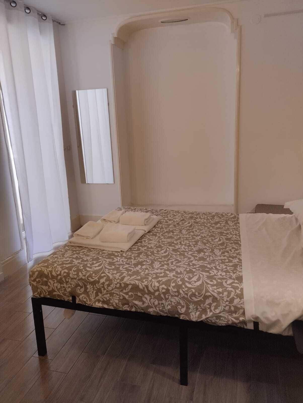 Un letto singolo con copriletto decorato, un comodino e uno specchio appeso al muro.