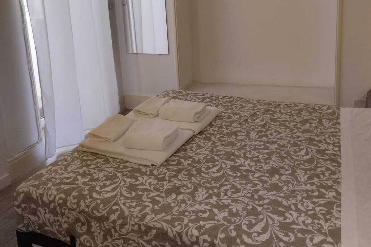 A hotel room with a bed, a mirror, and a window with curtains.