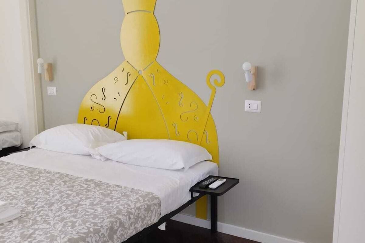 A bedroom with a bed, a nightstand, a wall-mounted light, and a wall decoration.