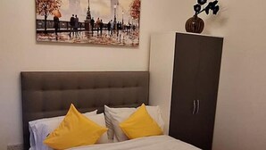 A bedroom with a bed, two yellow pillows, a grey headboard, a dark wardrobe, and a painting on the wall. - Flat 316 beautiful one bed apartment (Smethwick)