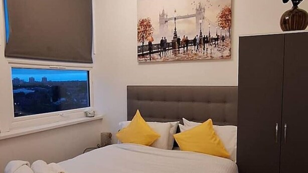 Habitación de hotel con cama, ventana con vista a un paisaje urbano, un cuadro de un puente y un armario.