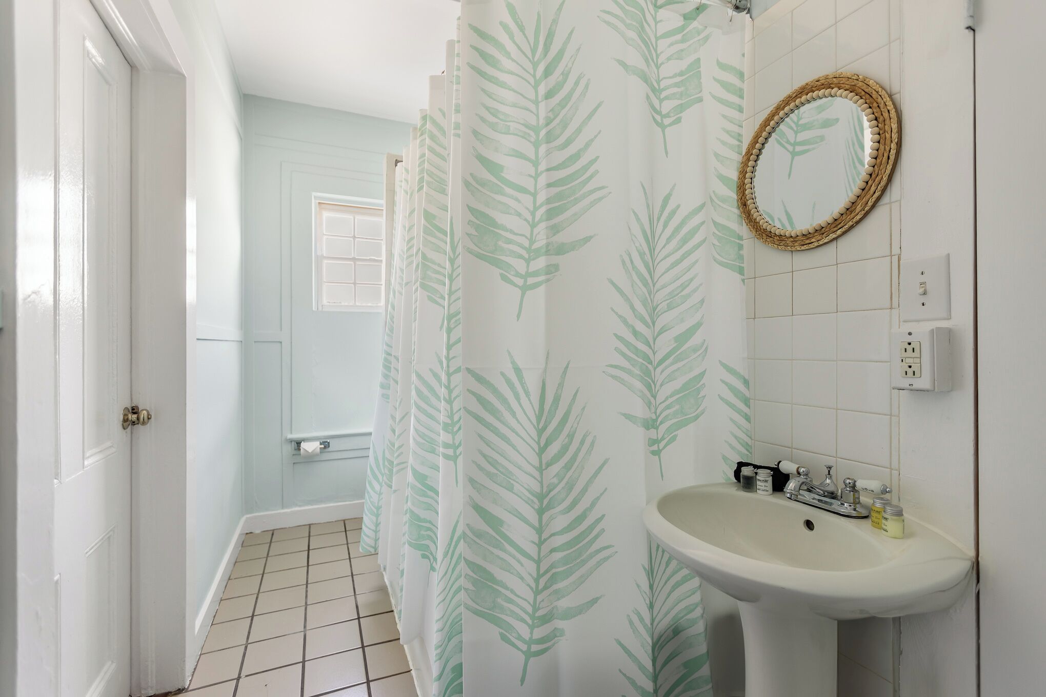 A bathroom with a white sink, a mirror with a wooden frame, and a shower curtain with a leaf pattern.