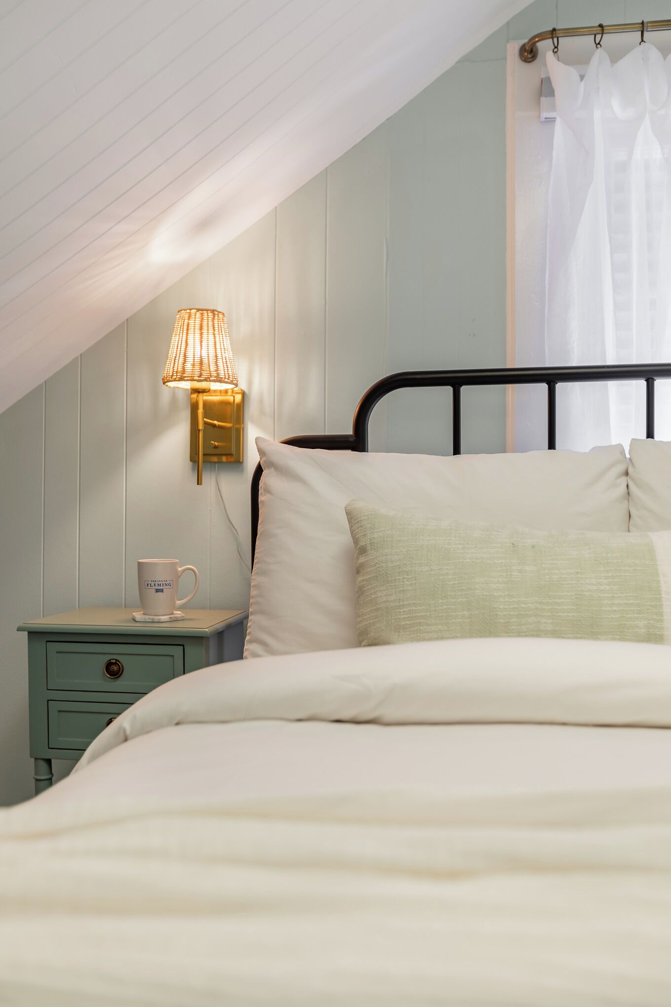 Un dormitorio con cama, mesita de noche, lámpara y ventana con cortinas.