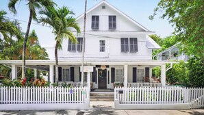 Une maison blanche à deux étages, dotée d’un porche, d’une clôture en piquets et d’une enseigne indiquant le numéro « 1016 ».