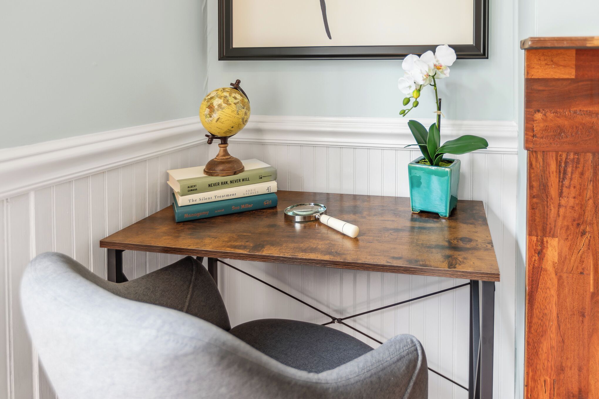 Une petite table en bois sur laquelle on trouve un globe terrestre, des livres, une loupe et une orchidée en pot.