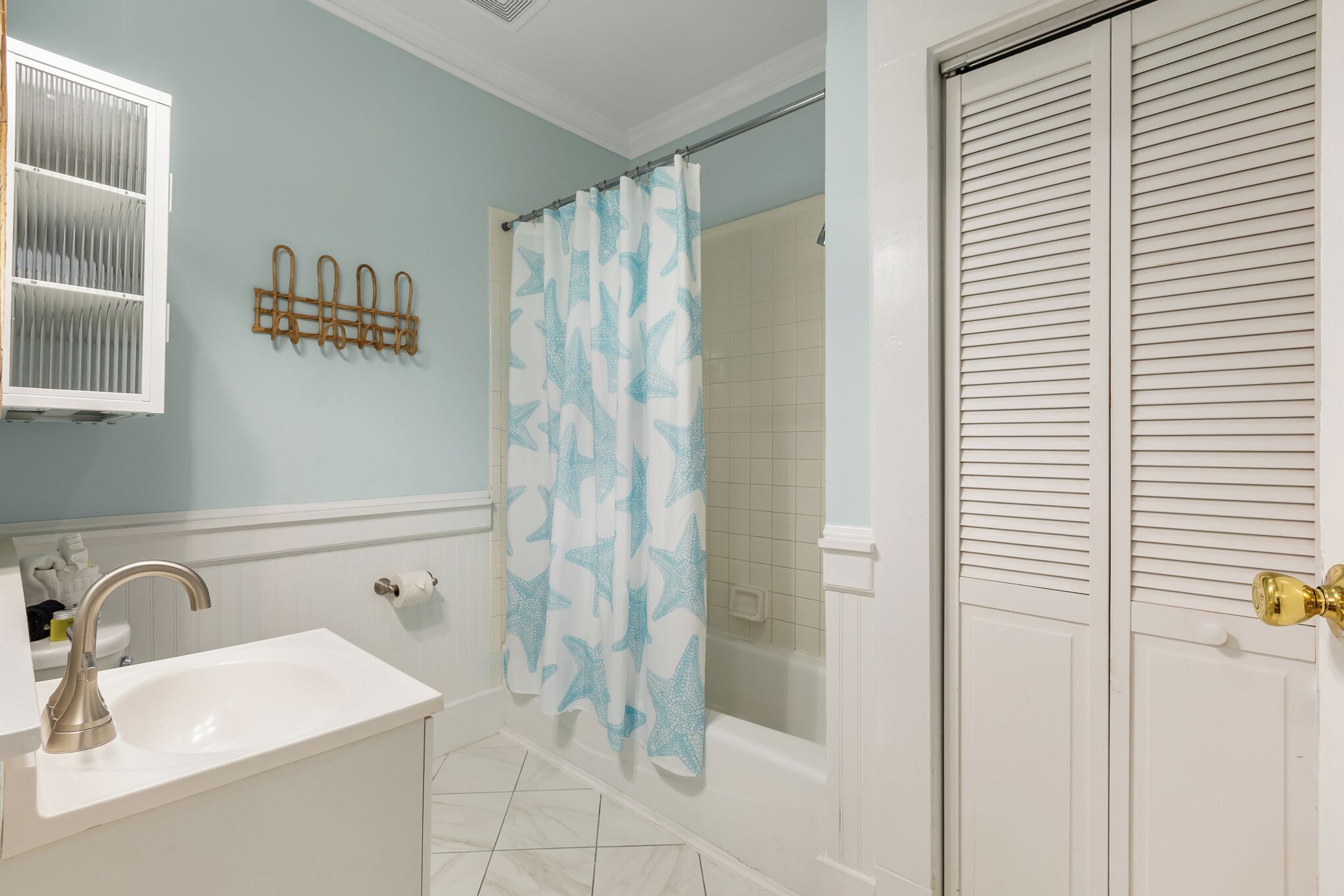 A bathroom with a sink, shower, and a white door with a gold handle.