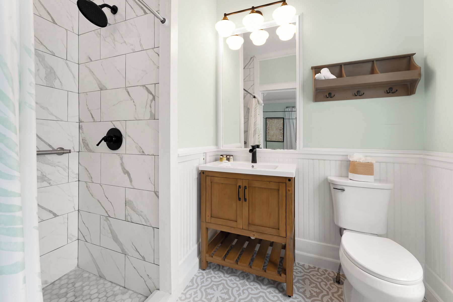 A bathroom with a shower, toilet, vanity, and a mirror with lights.