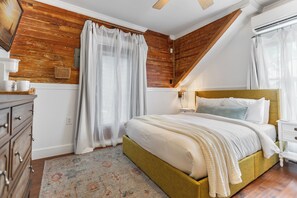 A bedroom with a wooden ceiling, a bed with white bedding, a nightstand, a dresser, and a patterned rug.