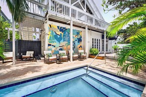 A pool area with a mural, outdoor seating, and a covered patio.